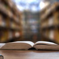 整然と並ぶ専門書と開かれた本がある書庫の風景。人事労務コラムの背景。