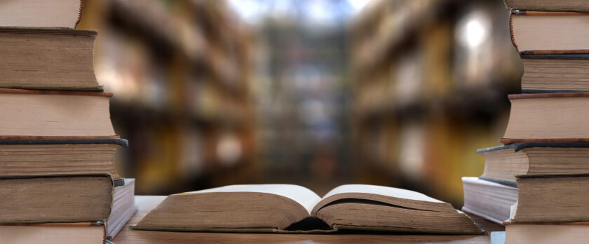 整然と並ぶ専門書と開かれた本がある書庫の風景。人事労務コラムの背景。